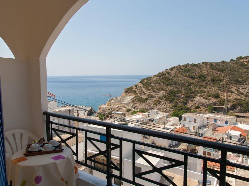 Balkon z stołem i krzesłem z widokiem na morze i wzgórza nadmorskiej wioski.