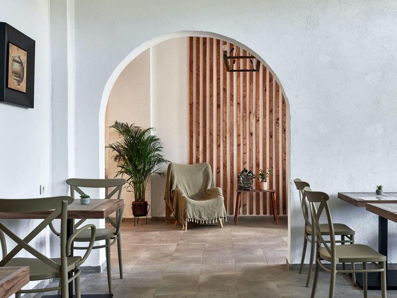 Nowoczesna, jasna sala jadalna z drewnianymi meblami, roślinami i łukiem w restauracji hotelowej.