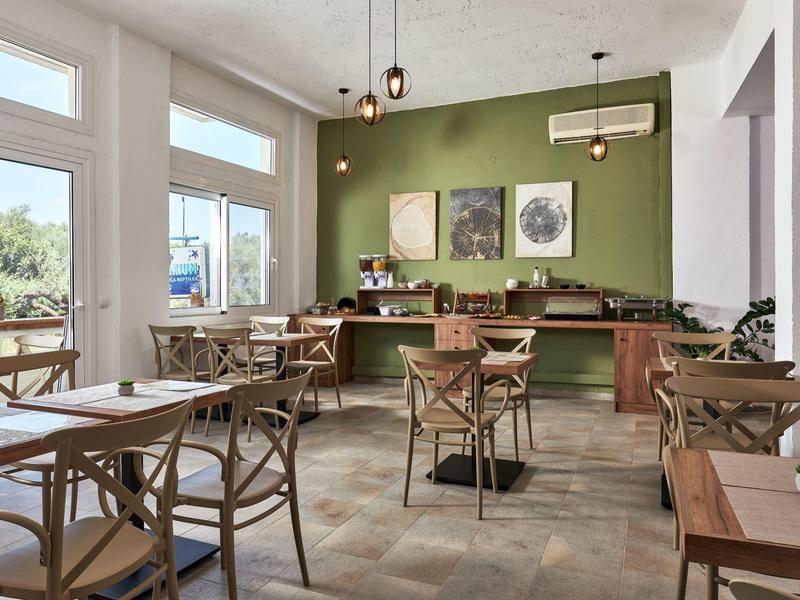 Jasna kawiarnia z drewnianymi stołami i krzesłami, zieloną ścianą i dużymi oknami.