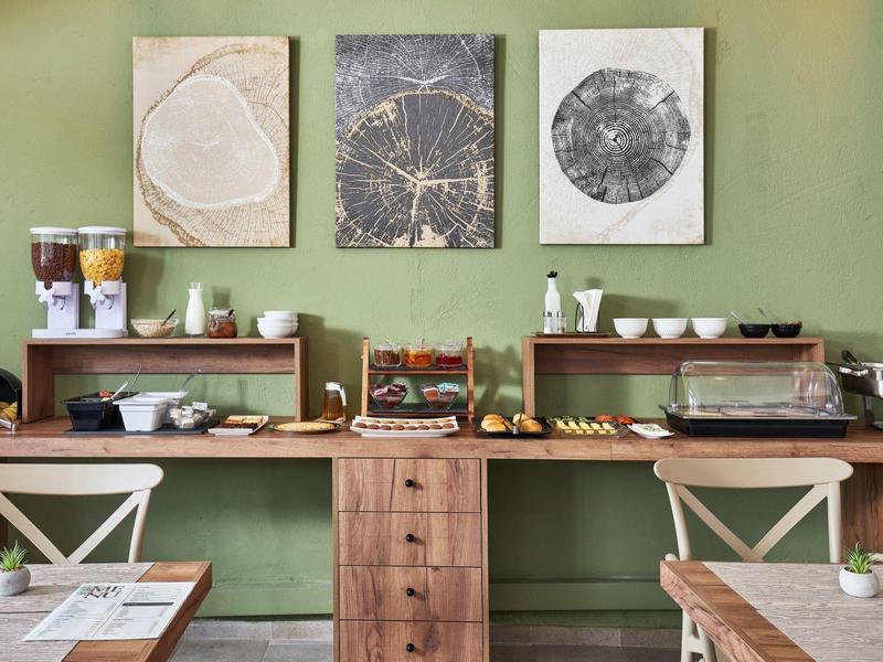 Bufet z płatkami, sokami i ciastkami na tle zielonej ściany w sali śniadaniowej hotelu