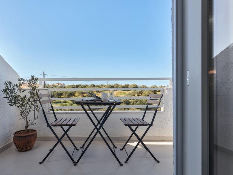 Balkon z małym czarnym stolikiem, dwoma krzesłami i widokiem na spokojny krajobraz.