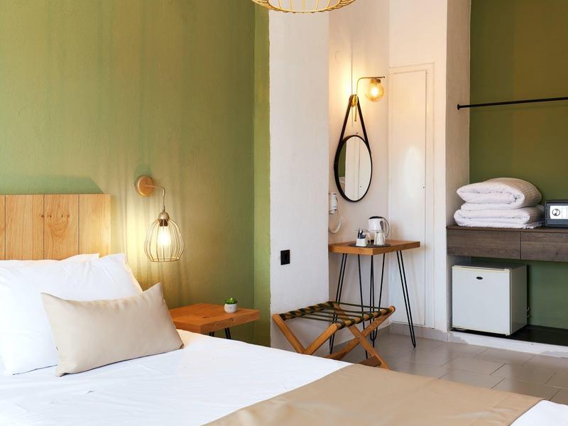 Sypialnia z zieloną ścianą, drewnianym łóżkiem, lustrem i miejscem do przechowywania w pokoju hotelowym.