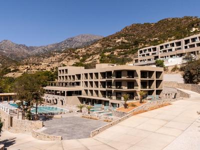 Grande hotel con piscina e terrazza in un paesaggio montano e arido sotto un cielo sereno.