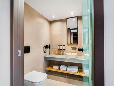 Moderne hotelbadkamer met douche, toilet, wastafel en handdoeken op de plank eronder.