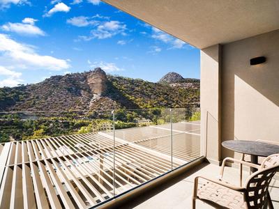 Balkon met tafel en stoelen met uitzicht op een beboste berg onder een blauwe lucht.