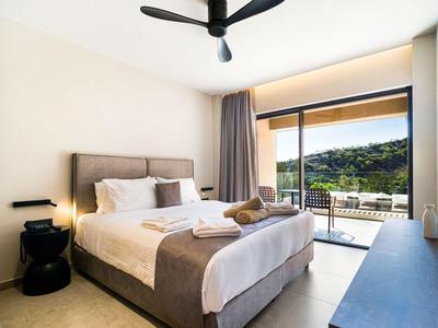 Lichte hotelkamer met tweepersoonsbed, plafondventilator en balkon met uitzicht op groene heuvels.