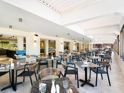 Ristorante moderno con molti tavoli e sedie, grandi finestre e illuminazione luminosa.