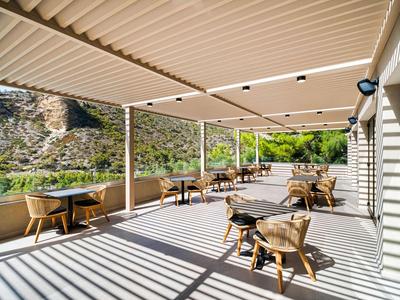 Terrasse ensoleillée avec chaises et tables sous un grand auvent blanc avec vue sur les montagnes.