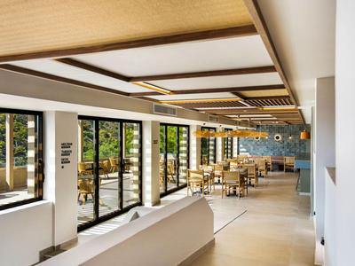 Lichte, moderne eetruimte met grote ramen en houten meubels, uitzicht op groene omgeving.