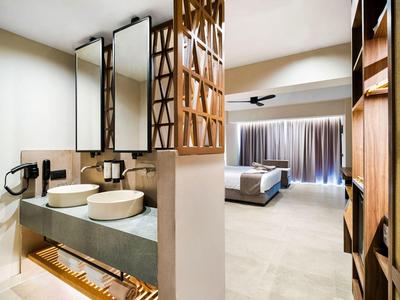 Moderne hotelkamer met open badkamer, wastafels en uitzicht op slaapkamer met groot bed en gordijnen.