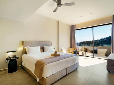 Modern hotelkamer met groot bed, plafondventilator en balkon met uitzicht.