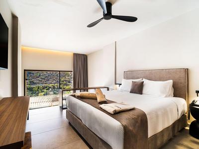 Chambre d'hôtel moderne avec grand lit, balcon et vue sur des collines verdoyantes.