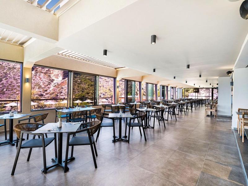 Ruime, lichte eetzaal met tafels en stoelen naast grote ramen met uitzicht op bloesems.