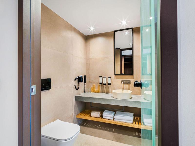 Moderne hotelbadkamer met douche, toilet, wastafel en handdoeken op de plank eronder.