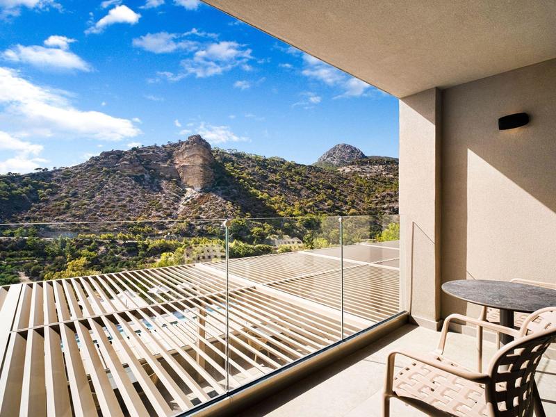 Balkon met tafel en stoelen met uitzicht op een beboste berg onder een blauwe lucht.