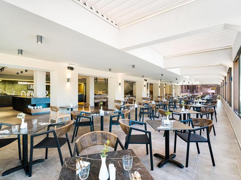 Moderne hotelrestaurant met veel tafels en stoelen naast grote ramen.