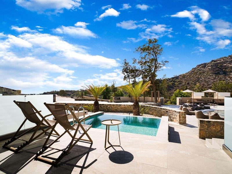Terras met zwembad, ligstoelen en bergzicht onder een heldere lucht.