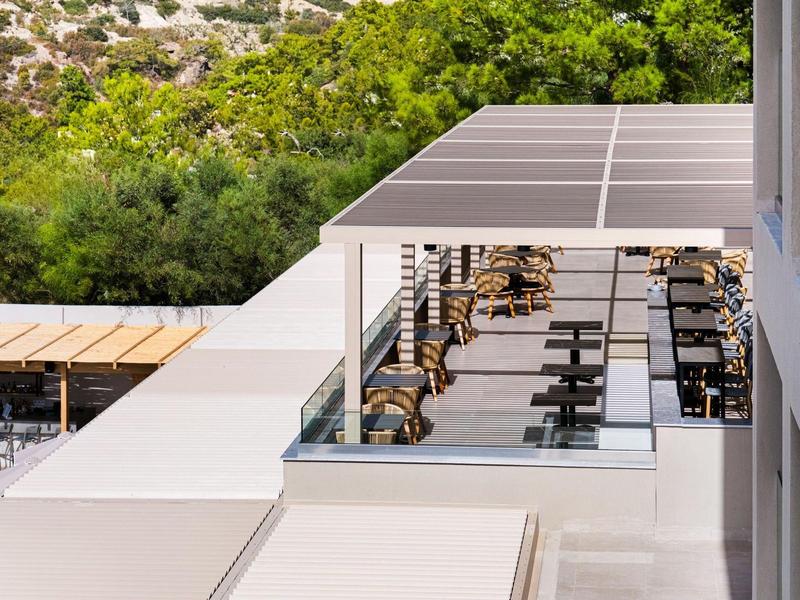 Modern open hotelbalkon met ligstoelen en witte parasols naast groene natuur.