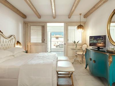 Camera d'hotel luminosa con letto matrimoniale, credenza turchese e balcone con vista mare.