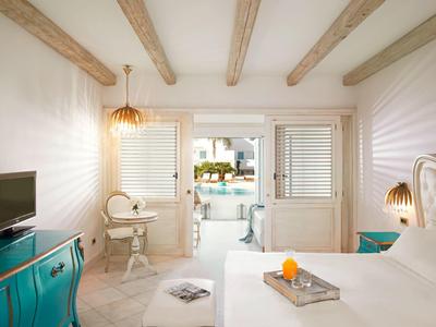Helles Schlafzimmer mit weißen Wänden, Holzbalken, hellblauem Sideboard und Zugang zu Terrasse.