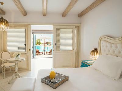 Helles Schlafzimmer mit weißem Bett, Holzbalkendecke und Blick auf Terrasse mit Pool.