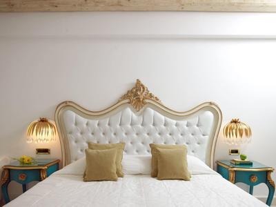 Elegantes Doppelbett mit weißem, gepolstertem Kopfteil, goldenen Verzierungen und grünen Nachttischen.