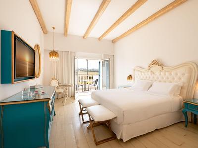 Světý hotelový pokoj s manželskou postelí, modrým nábytkem a balkonem s výhledem na moře.