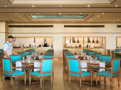 Elegantní restaurace s modrými židlemi a číšníkem připravujícím stůl.