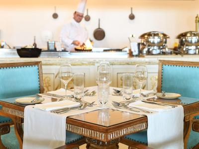 Elegantní jídelní stůl s modrými židlemi a kuchařem v pozadí v restauraci.