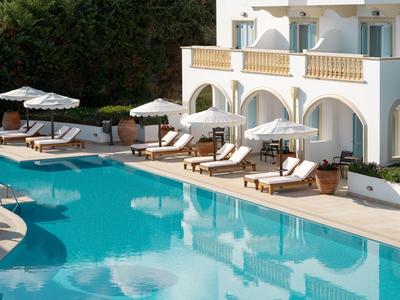 Hotel s bílou fasádou a bazénovou plochou s lehátky a slunečníky