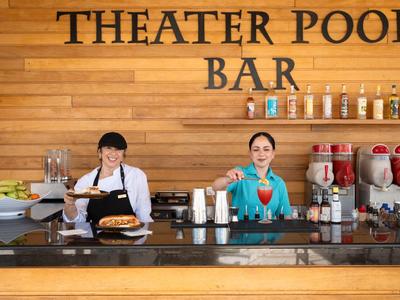 Dva barmani za barem s dřevěným obložením a nápisem THEATER POOL BAR