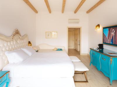 Světý hotelový pokoj s velkou postelí, modrým prádelníkem a televizí na stěně.