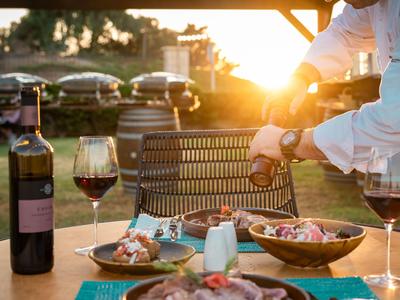 Večeře pod širým nebem za západu slunce s vínem a lahodným jídlem na dřevěném stole.