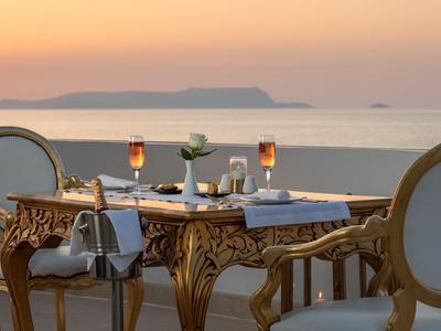 Elegantní stůl se dvěma sklenicemi na terase s výhledem na moře při západu slunce.