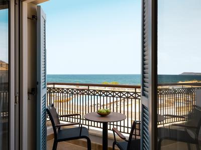 Balkon s stolem a židlemi s výhledem na moře a jasnou oblohu.