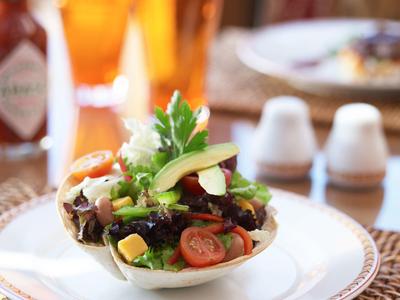 Teller mit Salat in Tortilla, Tomaten, Avocado und frischen Kräutern, beruhigender Hintergrund.