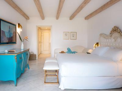 Světý hotelový pokoj se dvěma postelemi, modrým příborníkem a dřevěnými trámy na stropě.