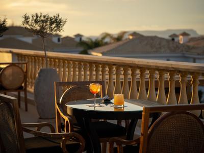 Večerní balkonová terasa se stolem, židlemi a nápoji při západu slunce.