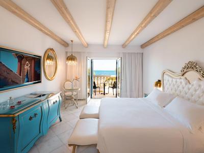 Světý hotelový pokoj s elegantním nábytkem, postelí king-size a výhledem na terasu a moře.