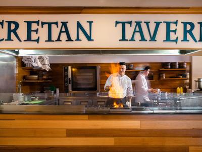 Kuchař v moderní řecké taverně s dřevěnými prvky stojí za pultem.