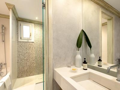 Světlá koupelna s umyvadlem, velkým zrcadlem a sprchovým koutem s bílými dlaždicemi.