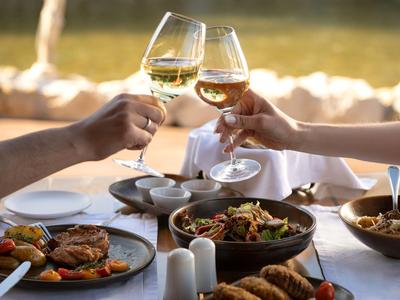 Dva lidé cinkají sklenicemi vína nad stolem plným různých jídel.