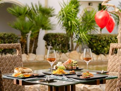 Stůl připravený s předkrmy a dvěma sklenicemi rosé před palmami a bílou zdí.