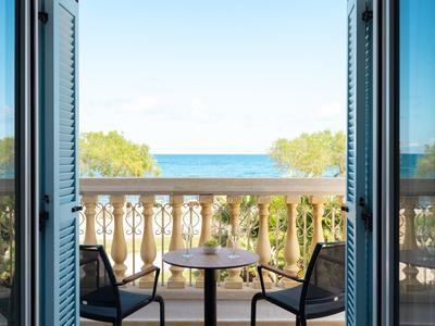 Balkon se dvěma židlemi a stolem s výhledem na moře a zalesněné pobřeží.