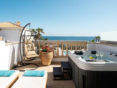 Terasa s vířivkou, závěsným křeslem a jasným výhledem na moře pod modrou oblohou.