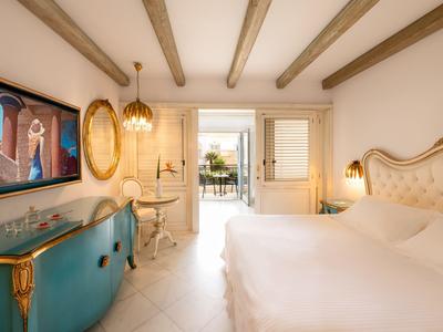 Elegantní hotelový pokoj s manželským lůžkem, modrou komodou a výhledem na slunnou terasu.