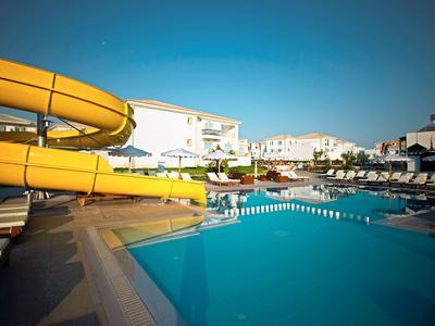 Čistý venkovní bazén se žlutou skluzavkou a lehátky pod modrou oblohou.