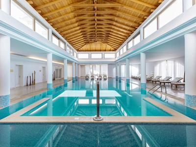 Vnitřní bazén v moderním hotelu s dřevěným stropem a několika lehátky.