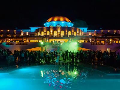 Osvětlený hotel s bazénem a lidmi v noci