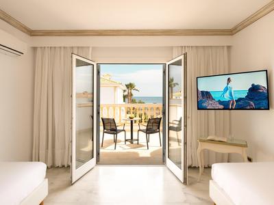 Světý hotelový pokoj s otevřeným balkonem a výhledem na moře.